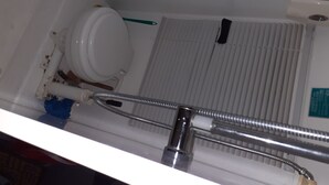 A bathroom with a toilet, a shower, and a visible pipe. - retro  housebus love (Waikanae)