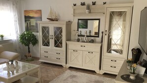 Una sala de estar con un sofá blanco, una mesa de centro de vidrio, un espejo grande y un mueble con cajones.