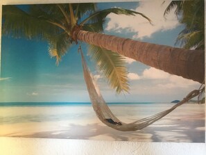 A hammock tied between palm trees on a beach with a clear sky.