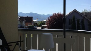 Un balcón con una mesa y un paraguas blanco, con vistas a una zona residencial y montañas.