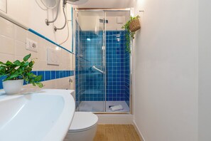 A bathroom with a glass-enclosed shower, a white sink, and a potted plant.