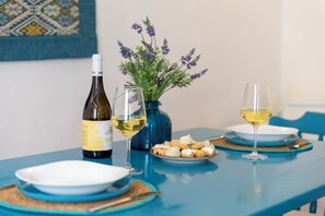A table with a bottle of wine, two glasses, a plate of food, and a vase with flowers.