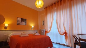A hotel room with a bed, two wall-mounted lamps, a large mirror, and sheer curtains.