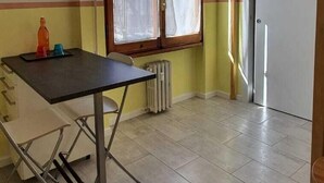 A small, bright kitchen with a table and chairs, a window with curtains, and a radiator.
