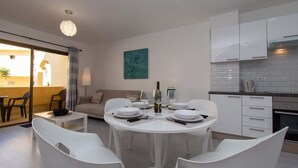 Une cuisine moderne avec des meubles blancs, un coin repas avec des chaises blanches et un salon avec un canapé et un tableau au mur.