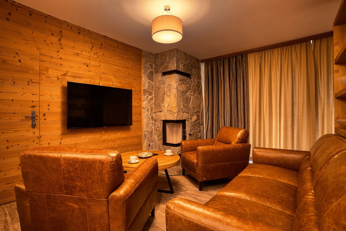 A cozy living room with leather sofas, a flat-screen TV, a stone accent wall, and a fireplace.