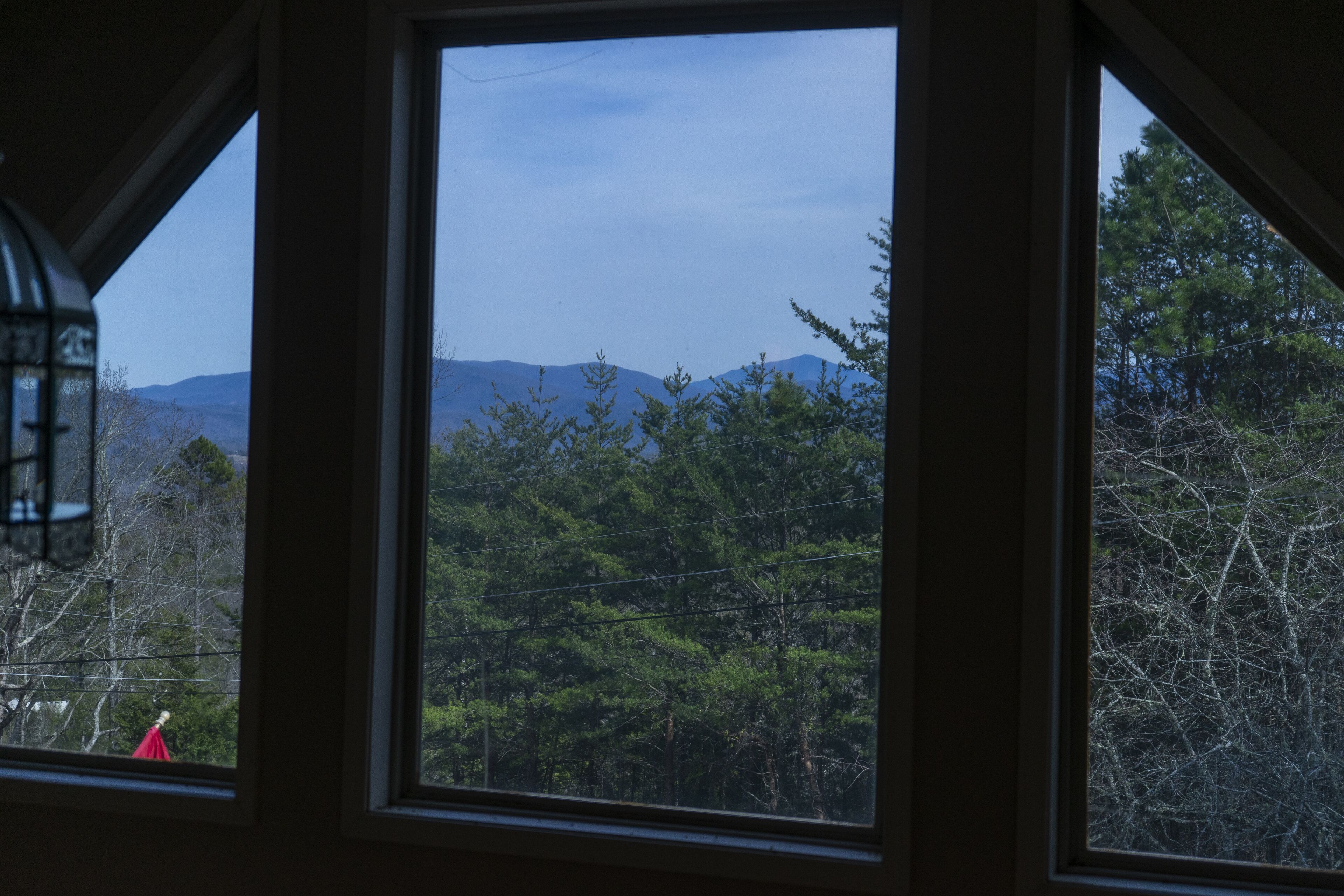A view through a window with a mountain landscape, including trees and power lines.
