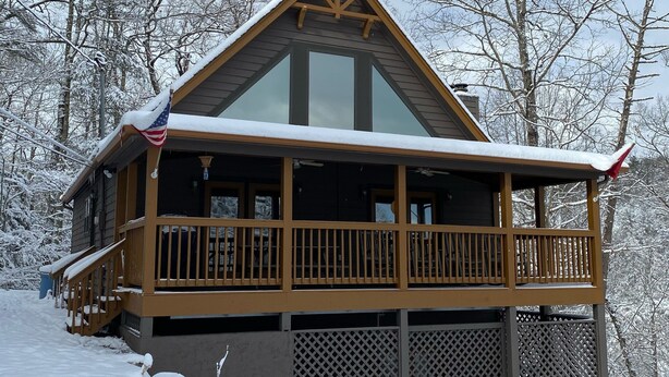 Une cabane dotée d’une grande façade vitrée, d’une terrasse en bois et offrant une vue sur un paysage enneigé.