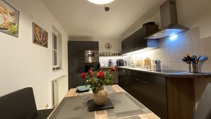 A modern kitchen with a dining area, featuring a clock, a vase with flowers, and various kitchen appliances. - "FeWO Gohrischblick" (Gohrisch)