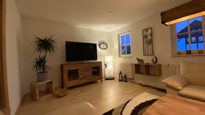 A living room with a TV, wooden cabinet, potted plant, and a large window. - "FeWO Gohrischblick" (Gohrisch)