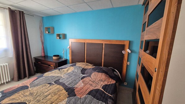 Une chambre à coucher comprenant un lit, une table de chevet, une commode, une fenêtre avec des rideaux et une armoire en bois.