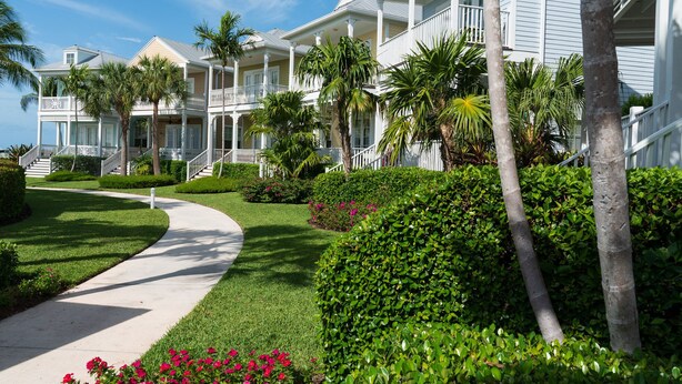 A multi-story hotel with a white exterior, a covered walkway, and lush greenery including palm trees and flowering plants. - Anglers Reef Islamorada  home with ocean views, private marina, beach & pool (Islamorada)
