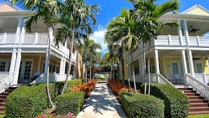 A hotel with a central pathway flanked by symmetrical landscaping and palm trees, leading to a covered porch area. - Anglers Reef Islamorada  home with ocean views, private marina, beach & pool (Islamorada)