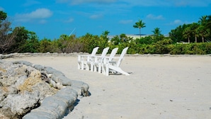 A sandy beach with white lounge chairs and a stone wall. - Anglers Reef Islamorada  home with ocean views, private marina, beach & pool (Islamorada)