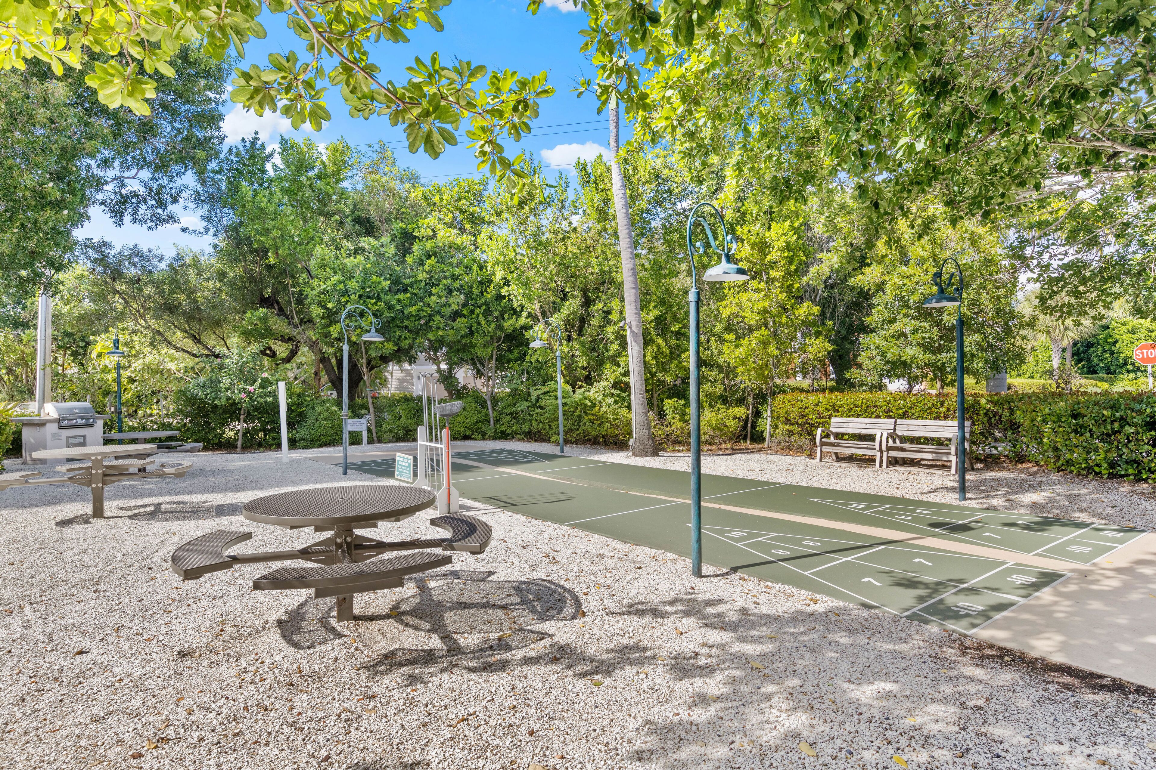 Un parque con cancha de baloncesto, mesas de picnic, una parrilla y un banco.