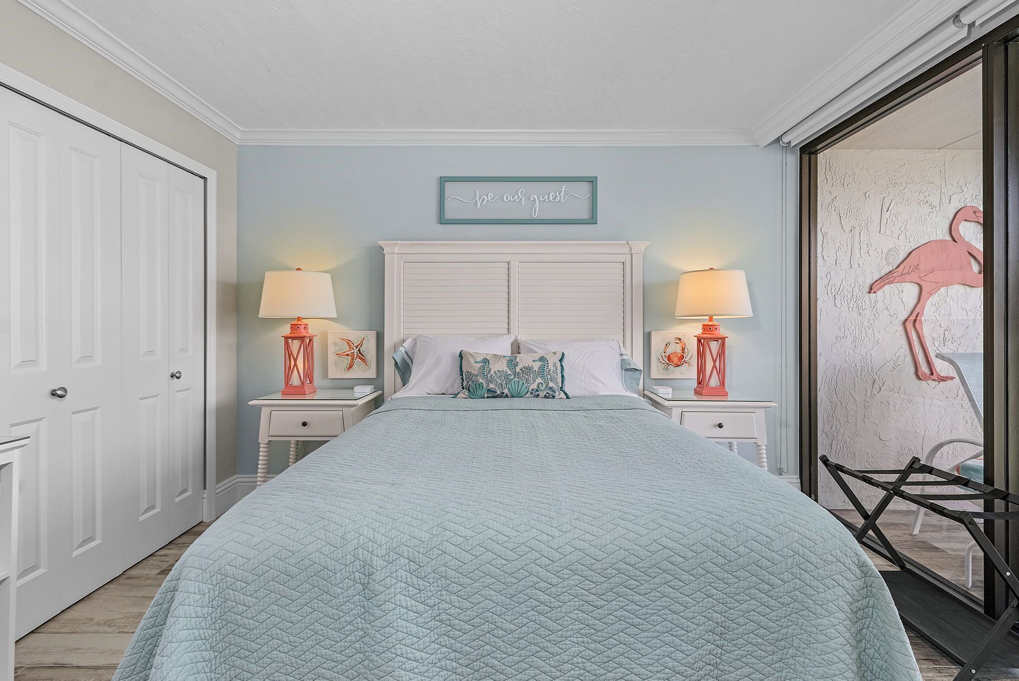A bedroom with a bed, two bedside tables with lamps, a wall sign, and a decorative wall piece.