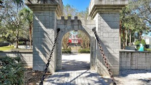 A stone archway with chains, leading to a building with a red roof.