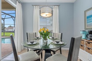 A dining area with a glass table, white curtains, and a view of a pool. - FROZEN,HARRY POTTER,MICKEY THEMED ROOMS,ENCANTO GAME ROOM 
5 MINUTES FROM DISNEY (Kissimmee)