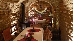 Un comedor acogedor con paredes de piedra, una chimenea y un árbol de Navidad. Las mesas están dispuestas con velas y un centro de mesa festivo.