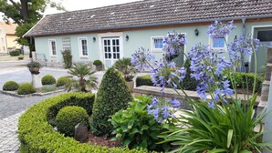 Una casa con techo de tejas, un porche delantero y un jardín con diversas plantas y flores.