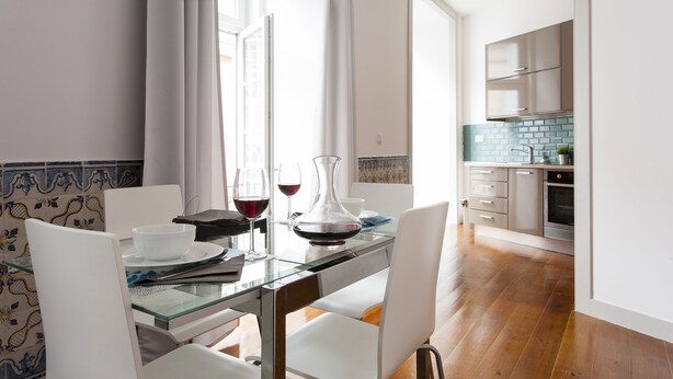 Un comedor con mesa de vidrio, sillas blancas y vista a la cocina.