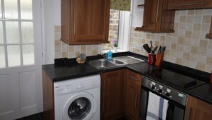 A kitchen with wooden cabinets, a washing machine, a stove, and a sink. - Stafford House (Sheffield)