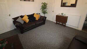 A living room with a dark brown sofa, a wooden side table, a mirror, and a radiator. - Stafford House (Sheffield)