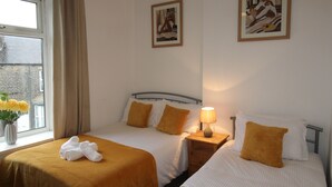 A hotel room with two beds, a window with curtains, a vase with flowers, and two framed pictures on the wall. - Stafford House (Sheffield)