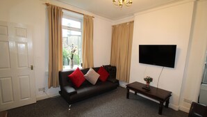 A living room with a dark leather sofa, a wooden coffee table, and a flat-screen TV mounted on the wall. - Stafford House (Sheffield)