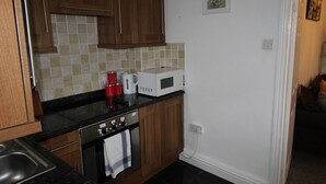 A kitchen with wooden cabinets, a black countertop, a white microwave, and a red coffee maker. - Stafford House (Sheffield)
