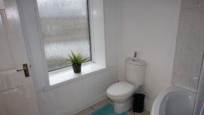 A bathroom with a toilet, a window with a plant, a bathtub, and a blue rug. - Stafford House (Sheffield)