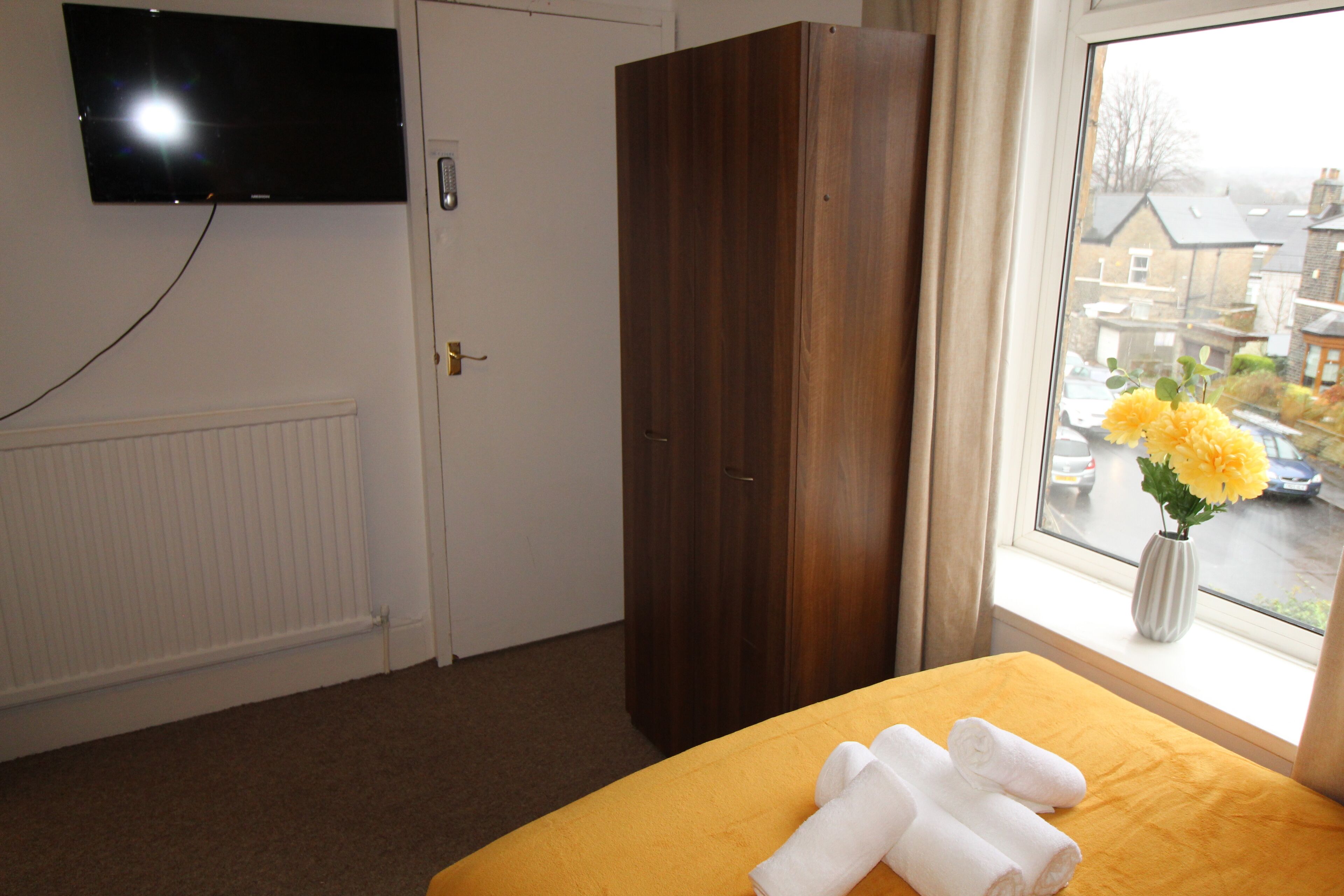 A hotel room with a bed, a wardrobe, a television mounted on the wall, and a window with a view of the street.