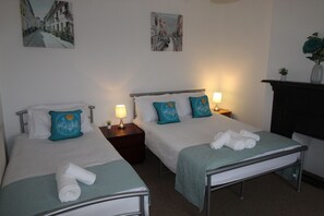 A hotel room with two single beds, each with a pillow and a lamp. There is a small table between the beds, and a fireplace on the right. - Stafford House (Sheffield)
