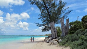 Ein Strand mit klarem türkisblauem Wasser, einem Sandstrand und zwei Personen, die spazieren gehen.