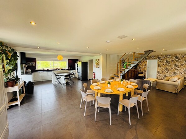 A spacious living area with a dining table set for six, a kitchen with modern appliances, and a staircase leading to an upper level.