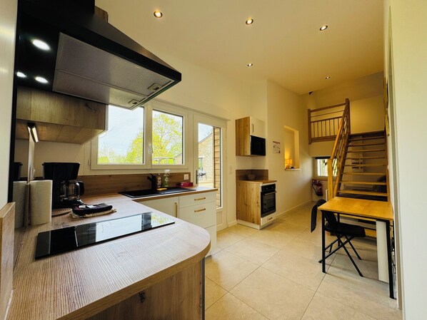 Een moderne keuken met een centraal eiland, een ingebouwde magnetron en een houten trap naar een hoger niveau.