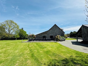 A stone building with a sloped roof, a paved driveway, and a grassy lawn.