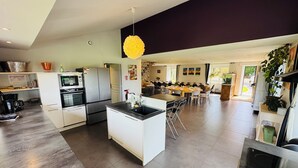 Una cocina moderna con una isla central, electrodomésticos integrados y un comedor con varias mesas.