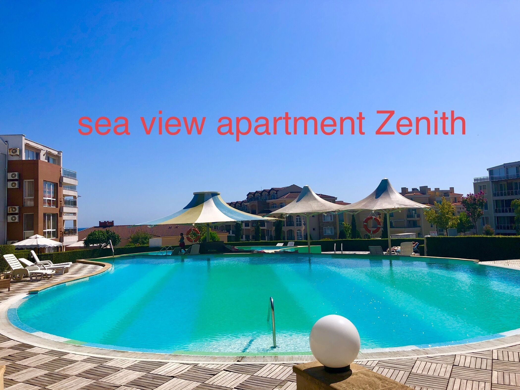 A sea view apartment with a pool, lounge chairs, and umbrellas.
