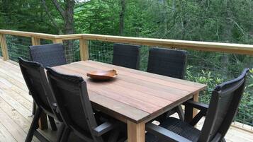 Une terrasse en bois, agrémentée d’une table et de chaises, entourée d’une balustrade en bois, et offrant une vue sur une zone boisée.