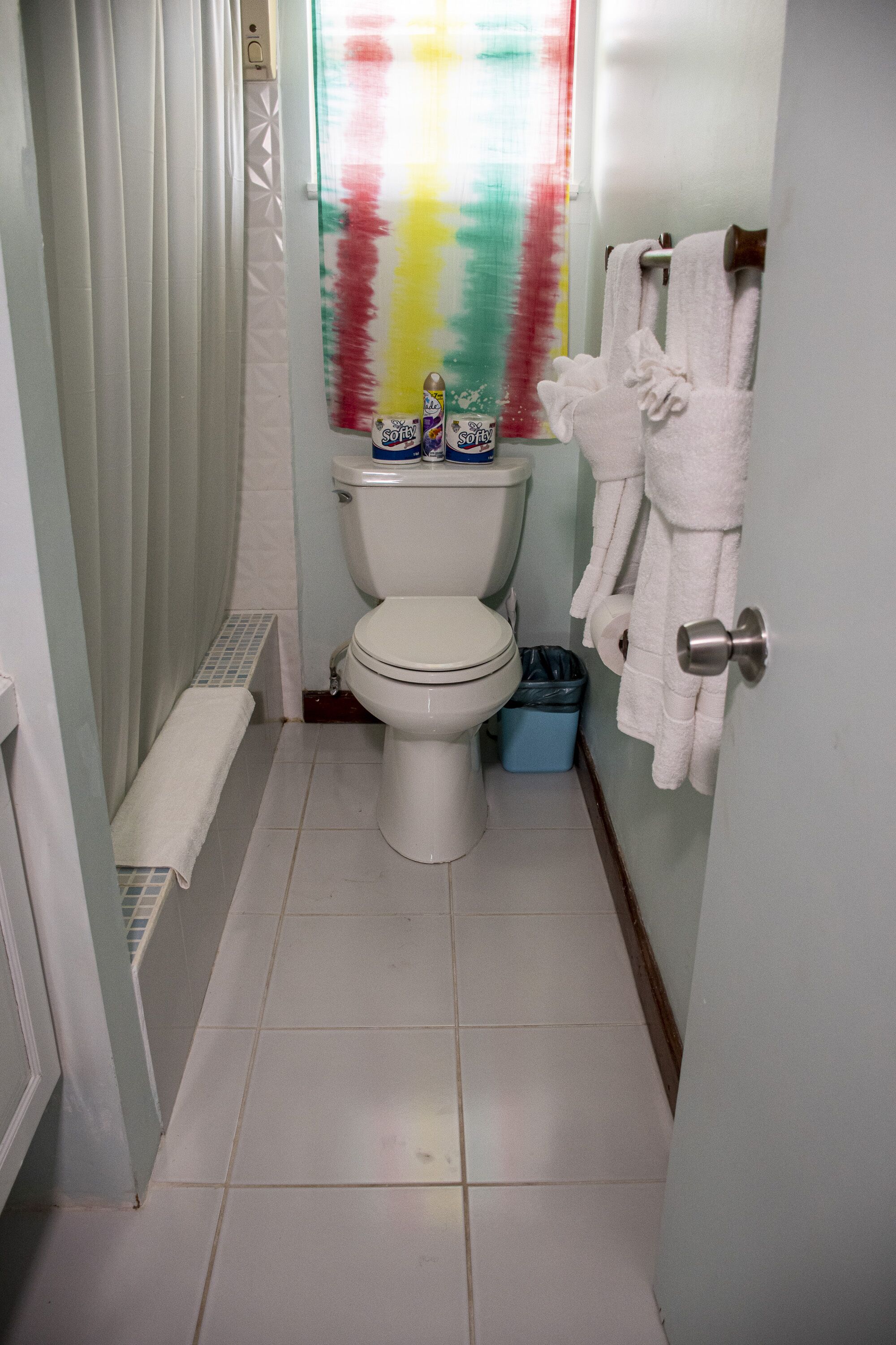 A small, narrow bathroom with a toilet, a shower curtain, and a towel rack with towels.