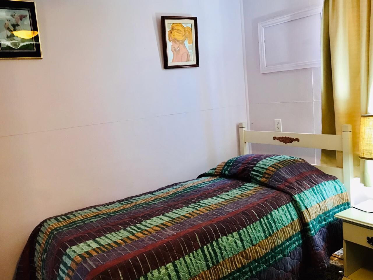 A single bed with a colorful striped bedspread, a framed picture on the wall, and a white headboard.