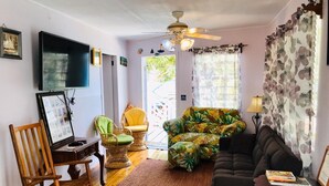 A living room with a flat-screen TV, a ceiling fan, a sofa, a chair, and a small table.