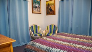 A bedroom with a bed, two striped chairs, a wooden table, and two framed pictures on the wall.