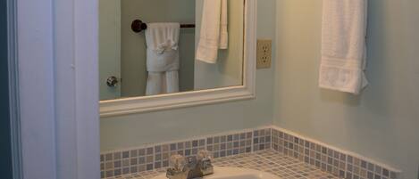 Un baño con un lavamanos blanco, un espejo con luces y dos toallas colgadas en ganchos.