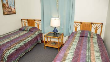 A room with two single beds, a small table with a lamp, and a painting on the wall.