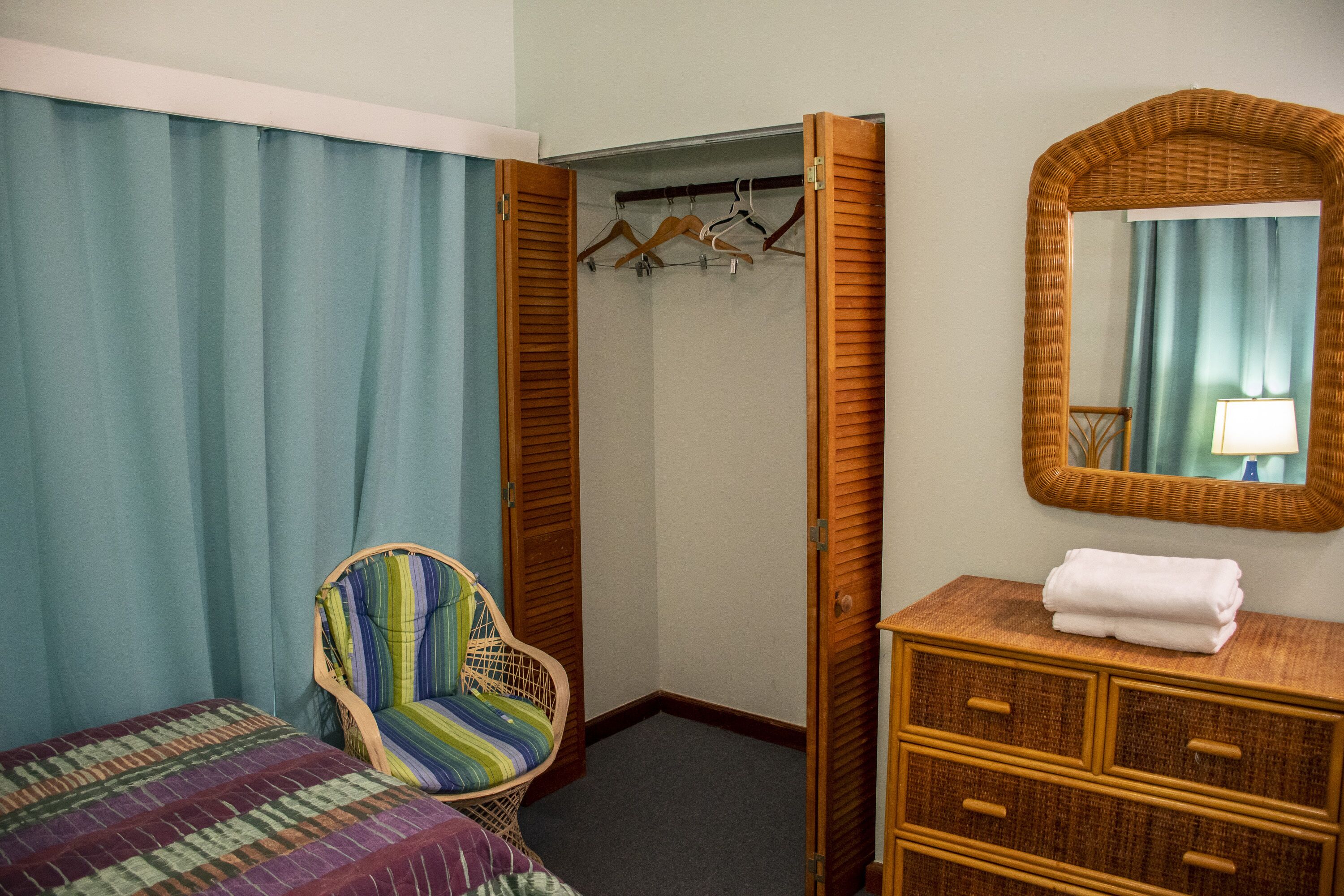 A bedroom with a bed, a striped chair, a wardrobe, and a mirror.