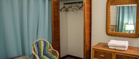 A bedroom with a bed, a striped chair, a wardrobe, and a mirror.