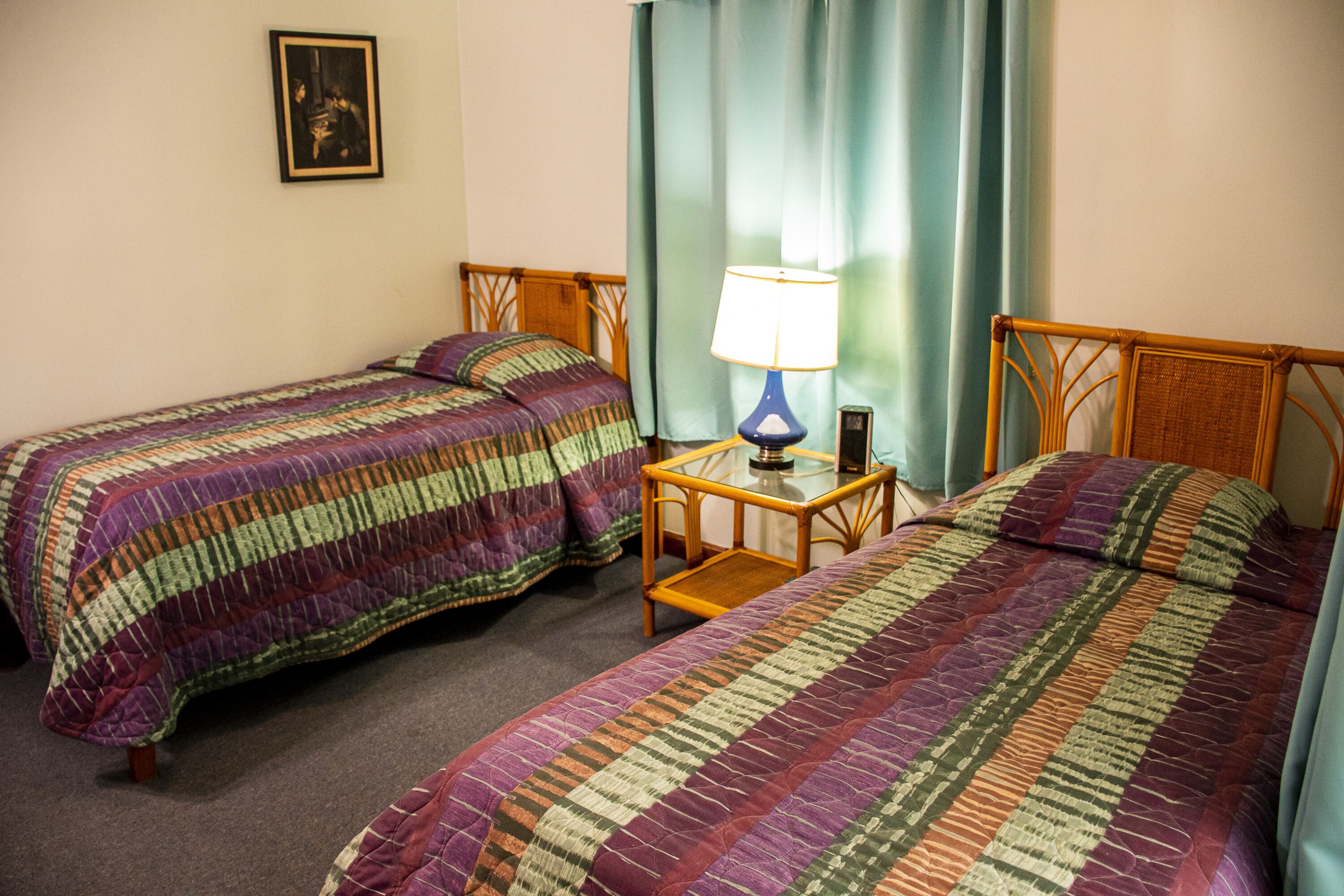 A hotel room with two single beds, a nightstand with a lamp, and a framed picture on the wall.