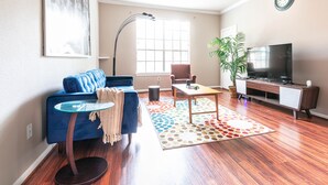 A living room with a blue sofa, a coffee table, a TV, a plant, and a ceiling fan. - COMFY COZY MED CENTER HOME (Houston)